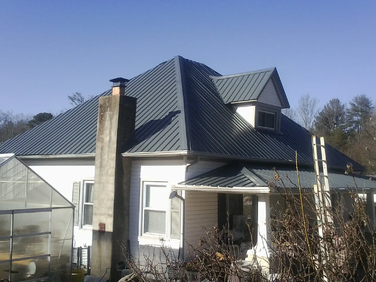 Dark blue standing seam metal roof on a white farmhouse with dormer — Slate & Tile Roof Repair by Roofing Brothers in Canisteo