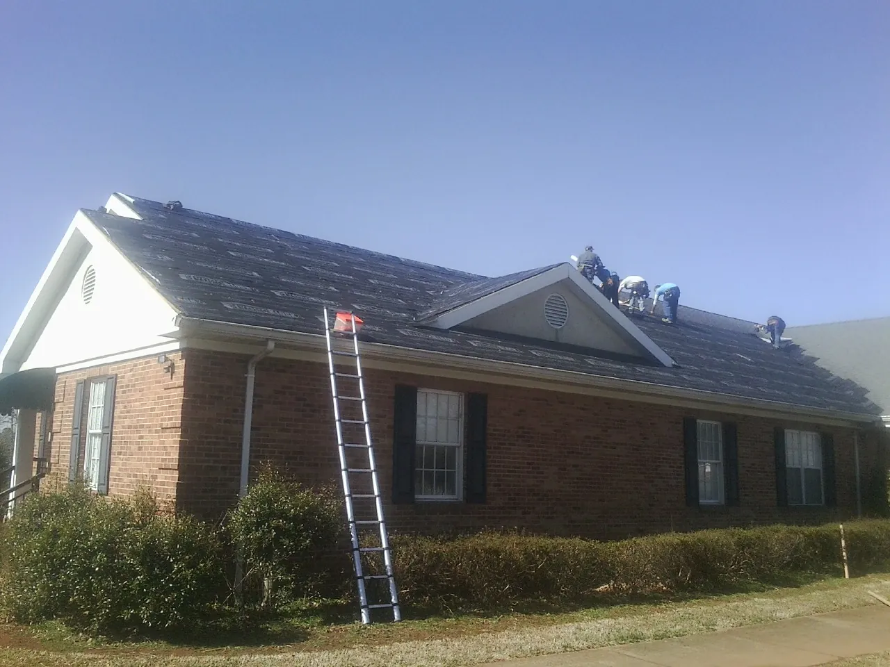 Crew tearing shingles off a brick ranch roof with a ladder set — Metal Roof Repair work by our crew in Canisteo