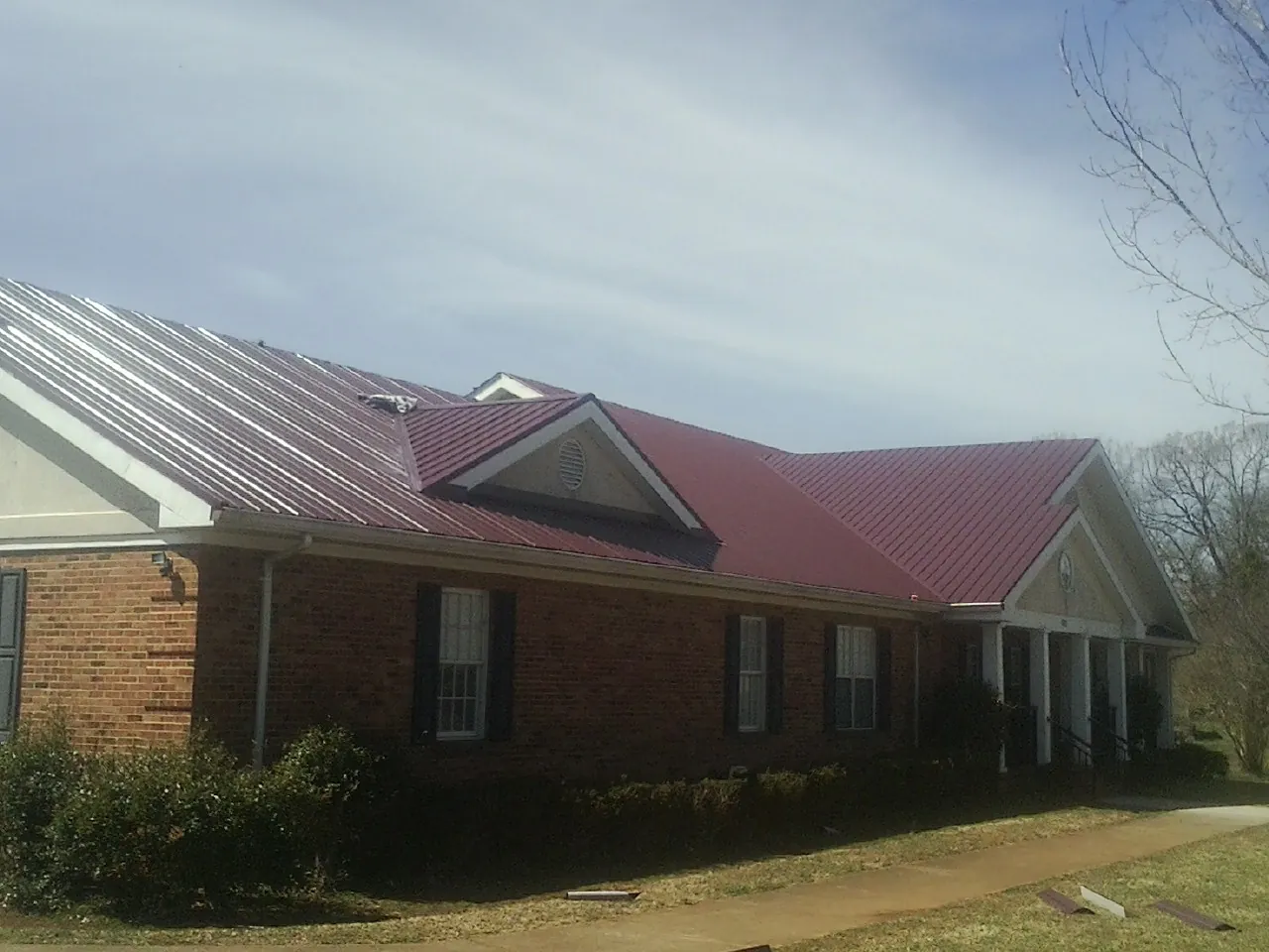 Red metal roof with gabled entries on a long brick building, from a Hail Damage Roof Repair job in Canisteo