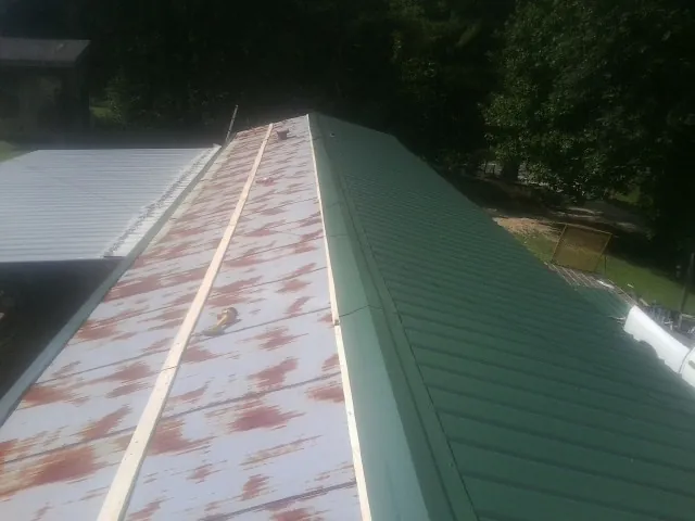 Old rusted panels beside newly installed green metal roofing — Wind Damage Roof Repair by Roofing Brothers in Canisteo