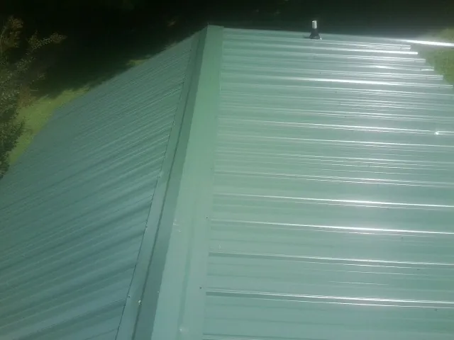 New green metal panels meeting at the ridge of a roof — Flat Roof Repair work by our crew in Canisteo