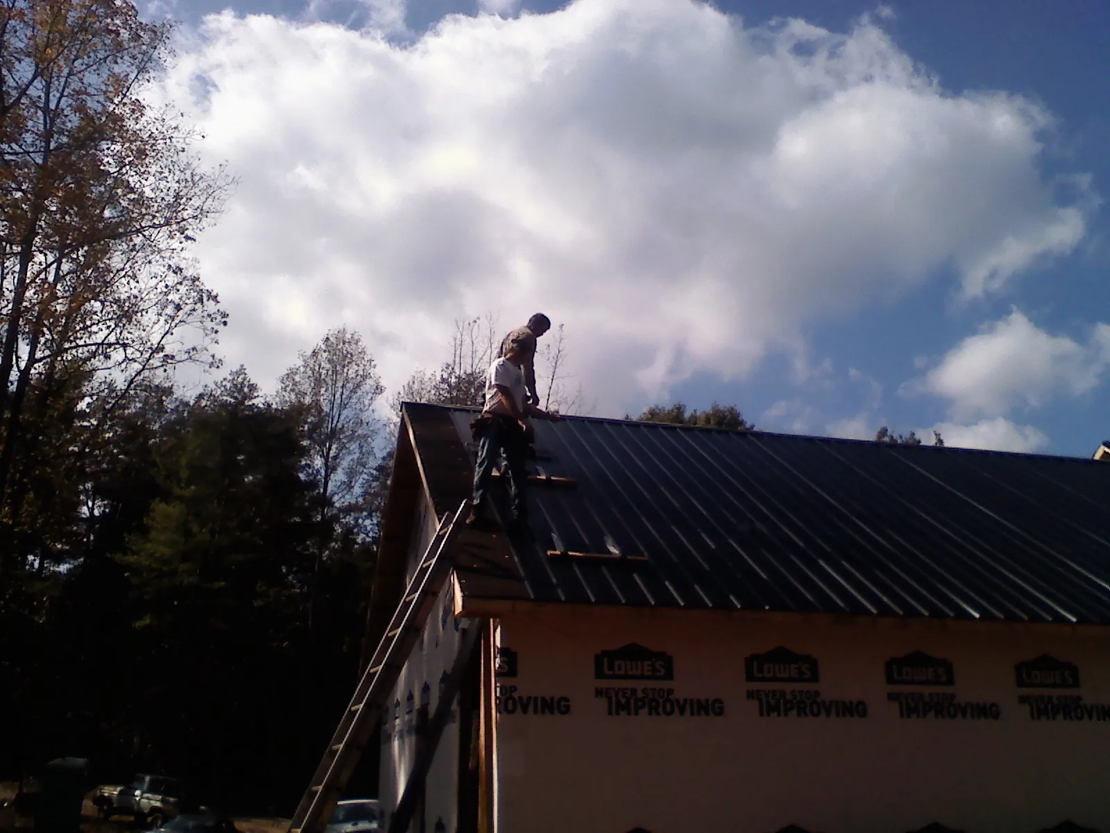 Roofer fastening dark metal panels high against a cloudy sky, from a Roof Inspection job in Canisteo