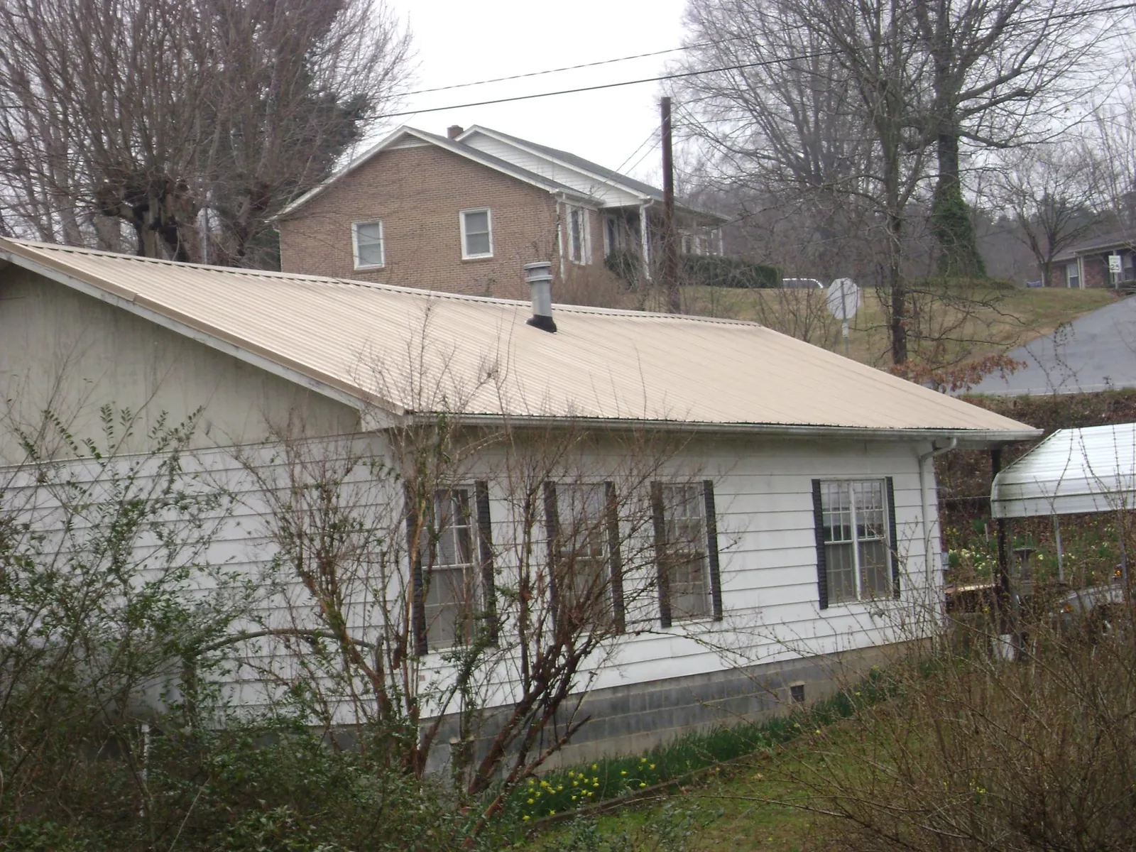 Tan metal roof on a white sided house set into a hillside — Commercial Roofing by Roofing Brothers in Canisteo